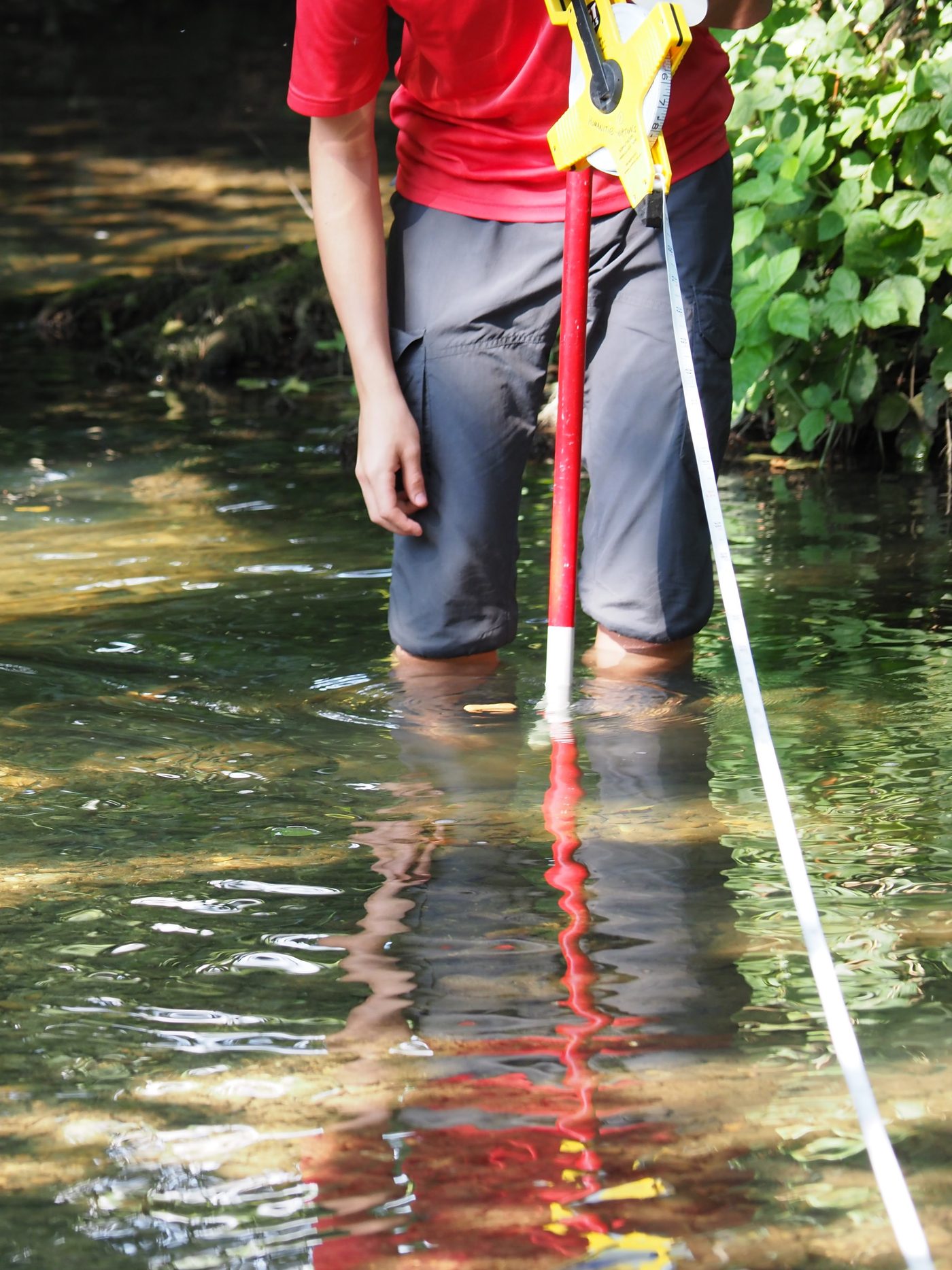 Measuring channel width with a tape and depth with a metre pole on the River Asse, annotated with the precautions that keep the readings comparable between sites